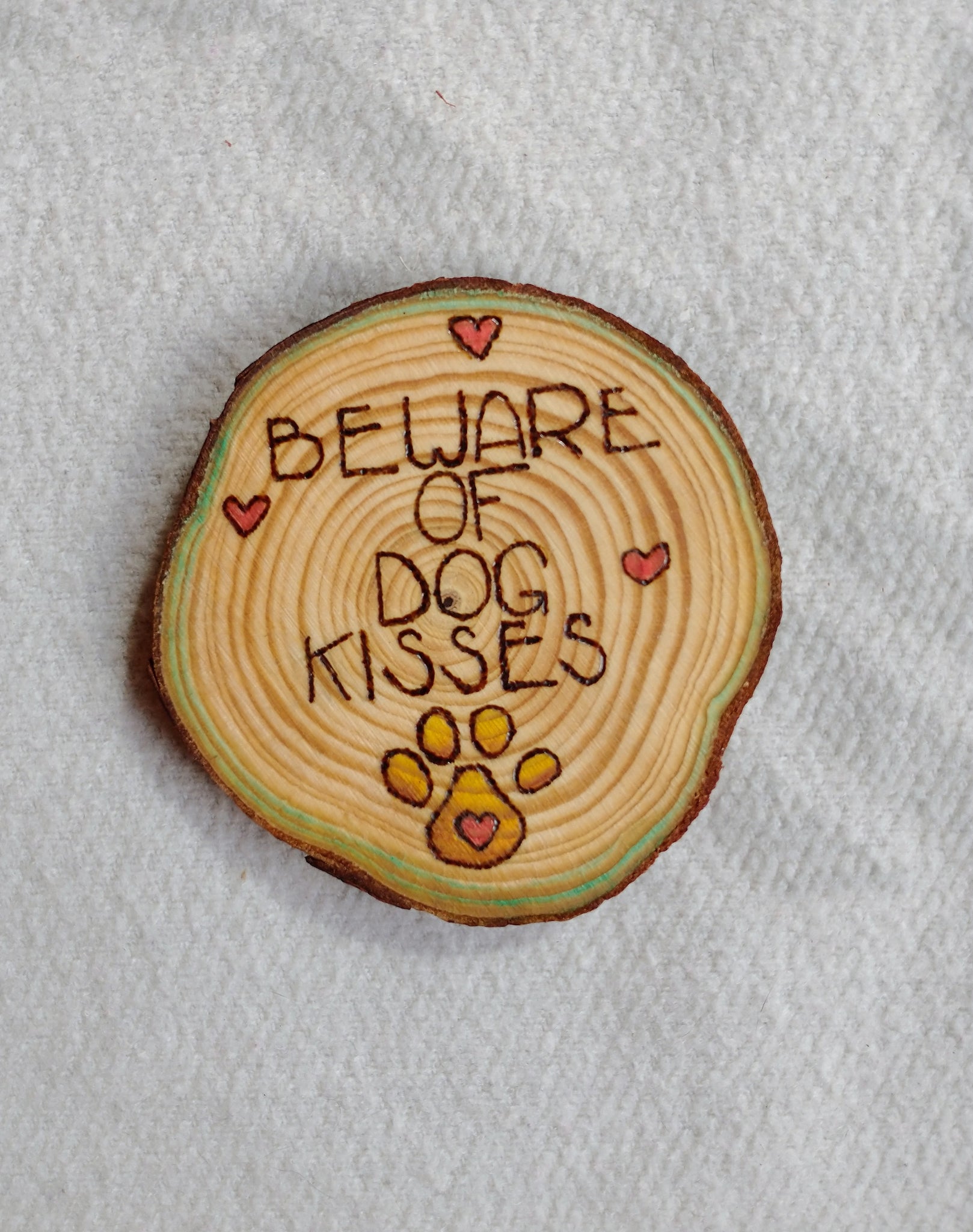 A wood slice coaster that has Beware of Dog Kisses wood burned onto it.