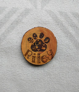 A wood slice coaster with a Custom Cat Paw Print and the name Riley wood burned into it. It is on a white background.