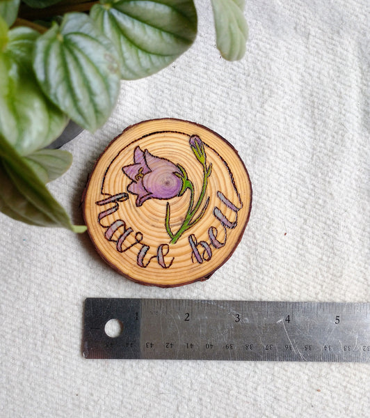 A Harebell Woodburned Wood Slice Ornament with a ruler underneath it to demonstrate its dimensions. 